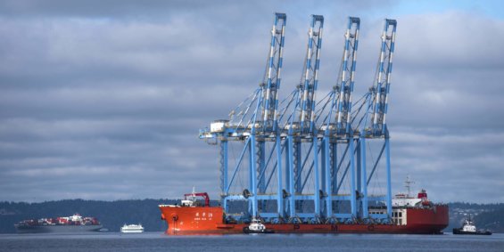 A large cargo ship carries industrial cranes in the Tacoma port